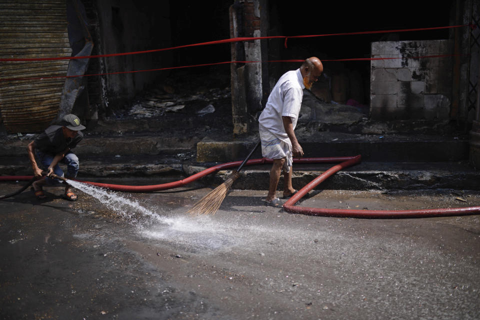 People wash a street after a fire swept through the area on Wednesday night in Dhaka, Bangladesh, Friday, Feb. 22, 2019. Police on Friday were seeking up to a dozen suspects in connection with a fire in the oldest part of Bangladesh's capital that killed scores of people. (AP Photo/Mahmud Hossain Opu )