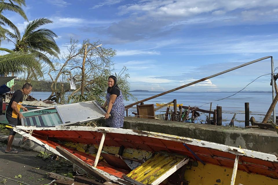 Residents carry what's left of their belongings as they walk past a damaged boat due to Typhoon Rai in Surigao city, Surigao del Norte, central Philippines on Friday Dec. 17, 2021. A powerful typhoon left more than a dozen people dead, knocked down power and communications in entire provinces and wrought widespread destruction mostly in the central Philippines, officials said Saturday. (AP Photo/Erwin Mascarinas)