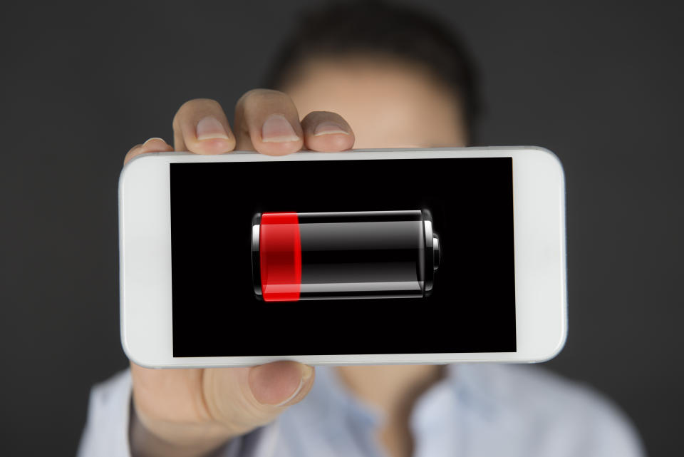 Woman showing a mobile phone with low battery icon in the screen.