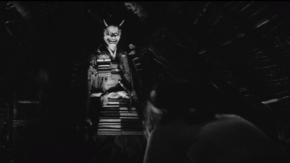 A samurai with a scary mask stands in a hut in Onibaba