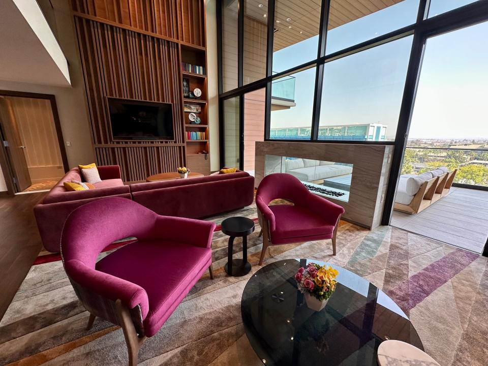 Living room in Disneyland grand villa with two-story windos, large built-in wood display with TV, and two burgundy chairs next to balcony