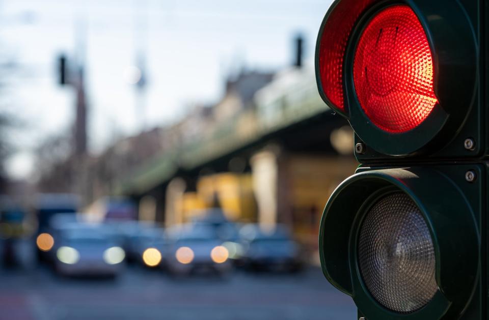 A traffic light shines red with several cars waiting in the background.