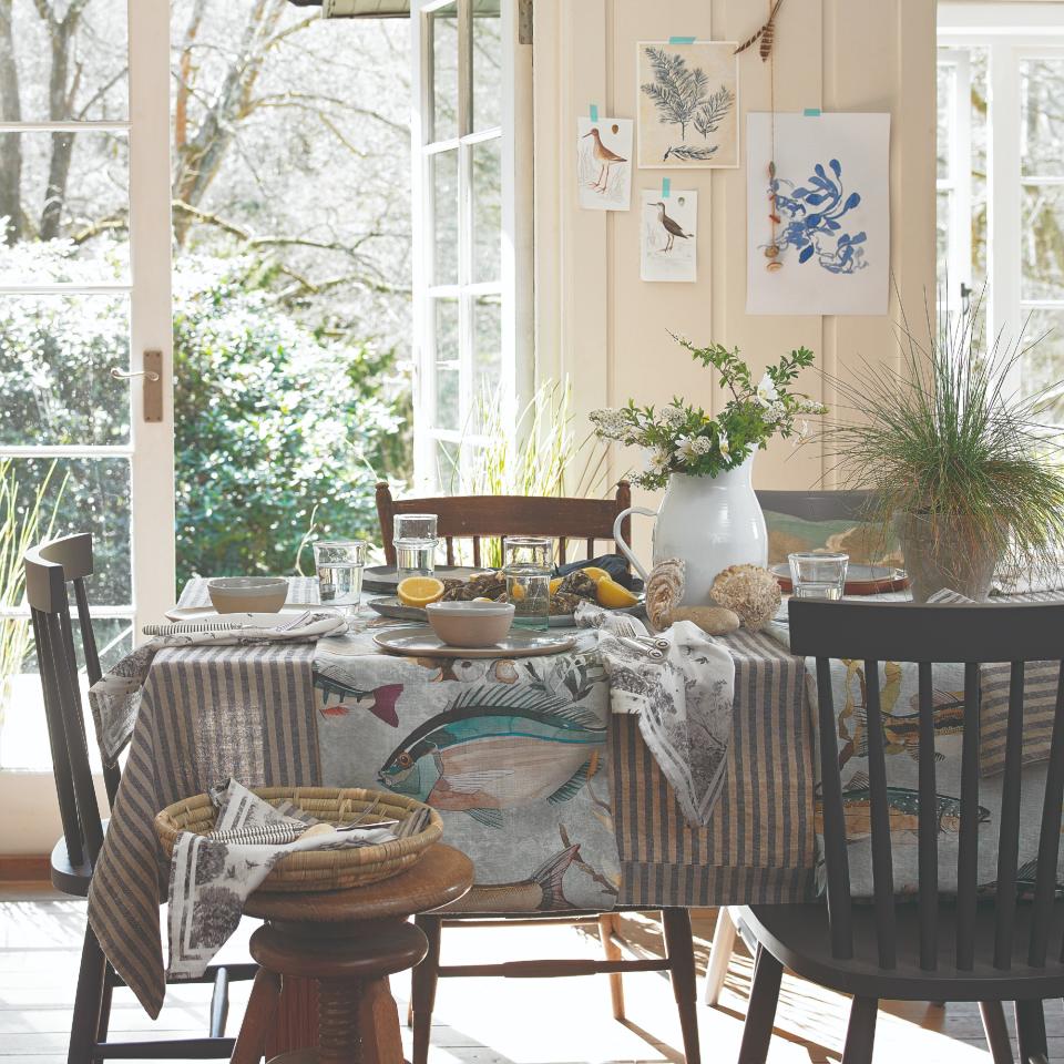 A set dining table with a thin striped tablecloth in white and blue and fish-print table runners