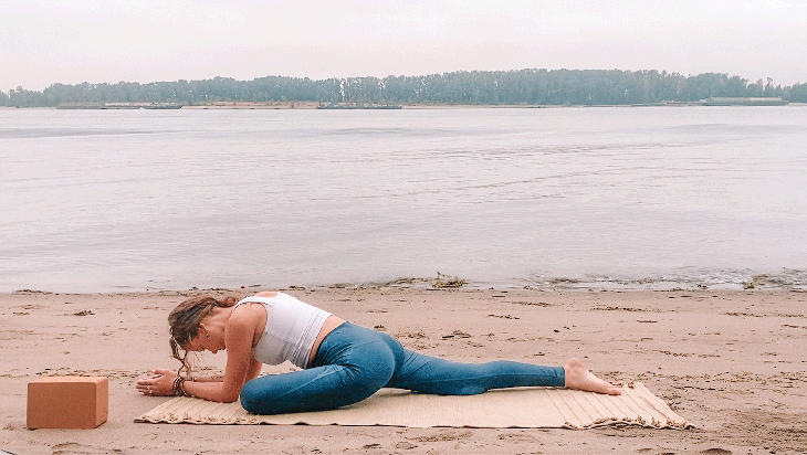 Woman lying on her belly with one knee bent and the other leg straight in Sleeping Swan, a Yin Yoga pose