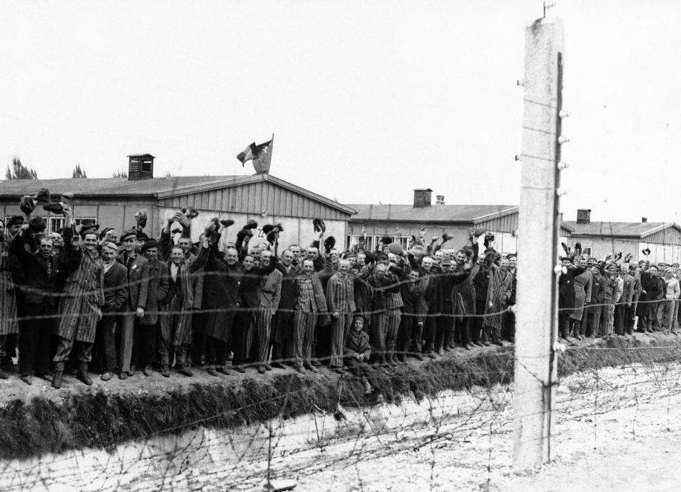 Prisoners at the electric fence of Dachau concentration camp cheer the Americans in Dachau, Germany in an undated photo. Some of them wear the striped blue and white prison garb. They decorated their huts with flags of all nations which they had made secretly as they heard the guns of the 42nd Rainbow Div., getting louder and louder on the approach to Dachau. (AP Photo)