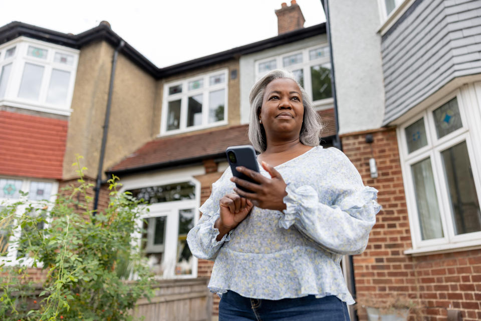 Mature woman outside her house ordering a taxi using an app on her cell phone - lifestyle concepts