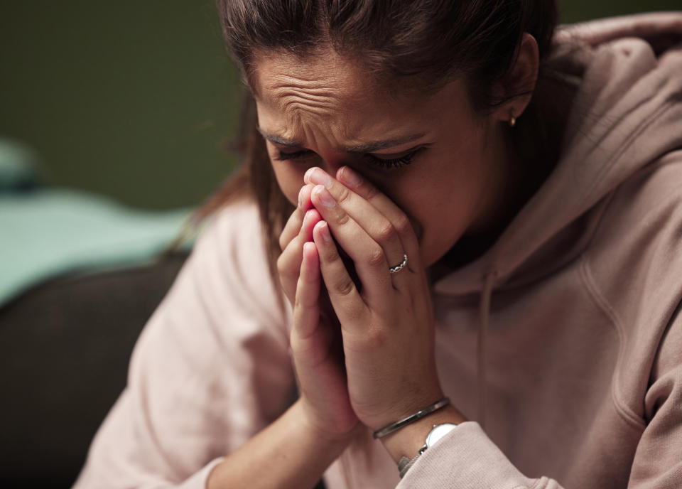 A person wearing a hoodie looks distressed, covering their nose and mouth with their hands, appearing to be crying or in deep thought