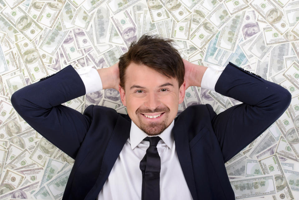 A wealthy businessman in a suit lying on a bed of cash.