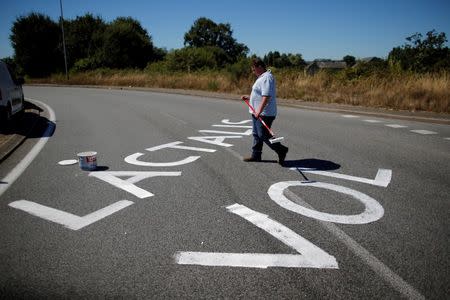 A French dairy farmer writes a message on the road as farmers from the FNSEA union gather to block the round-about access to the Lactalis plant in protest against the price of milk in Laval, France, August 23, 2016. REUTERS/Stephane Mahe