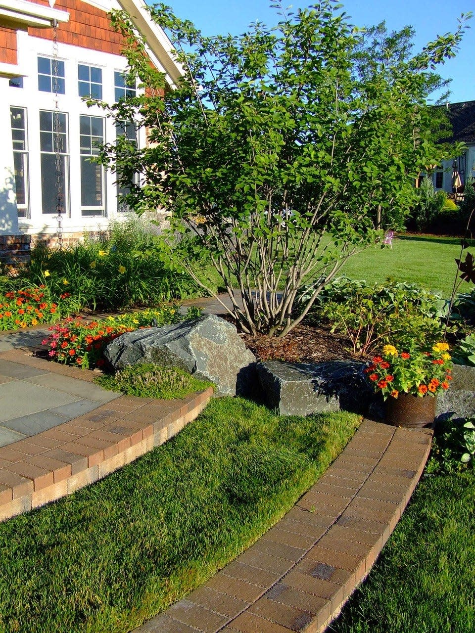 At a home in Delafield, gunmetal boulders from north central Wisconsin “shoulder in” custom lawn terrace steps and transition the adjacent grade.