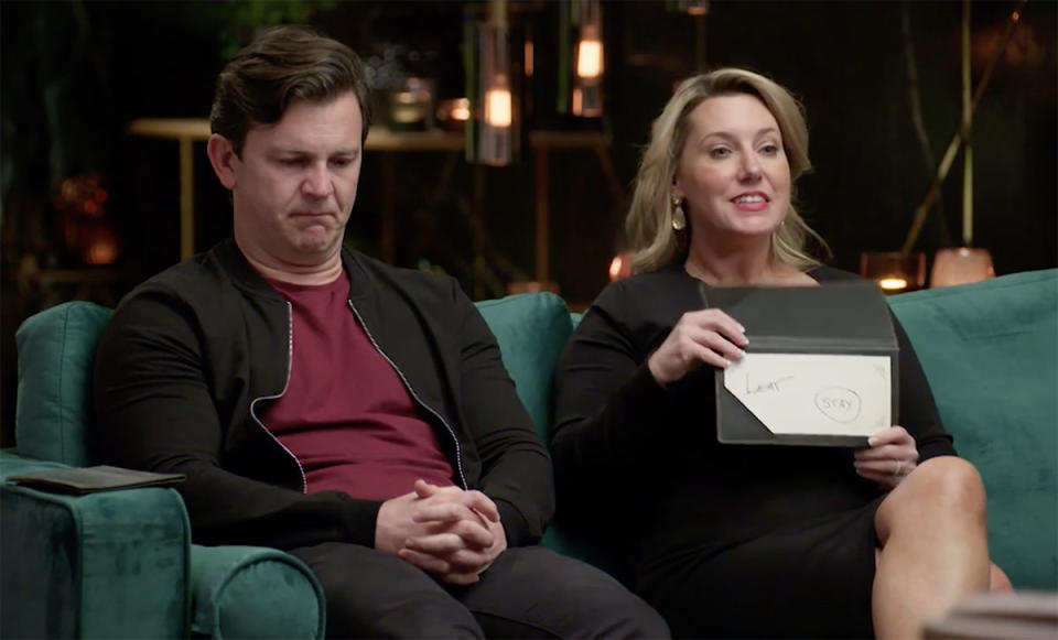 Josh looking sad on the MAFS couch while Melissa looks happy and shows her card saying 'stay'.