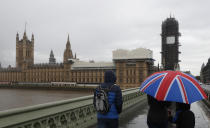 Tourists sheltering underneath a British Union flag umbrella walk across Westminster Bridge in the rain towards the Houses of Parliament in London, Thursday, Oct. 17, 2019. (AP Photo/Alastair Grant)