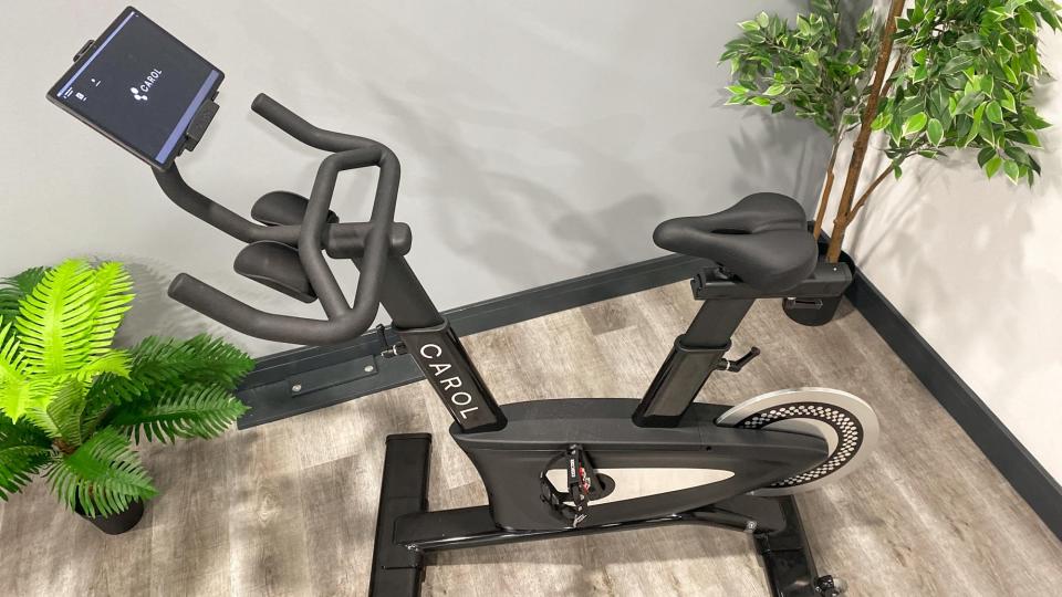 the CAROL 2.0 exercise bike in the corner of a room surrounded by houseplants