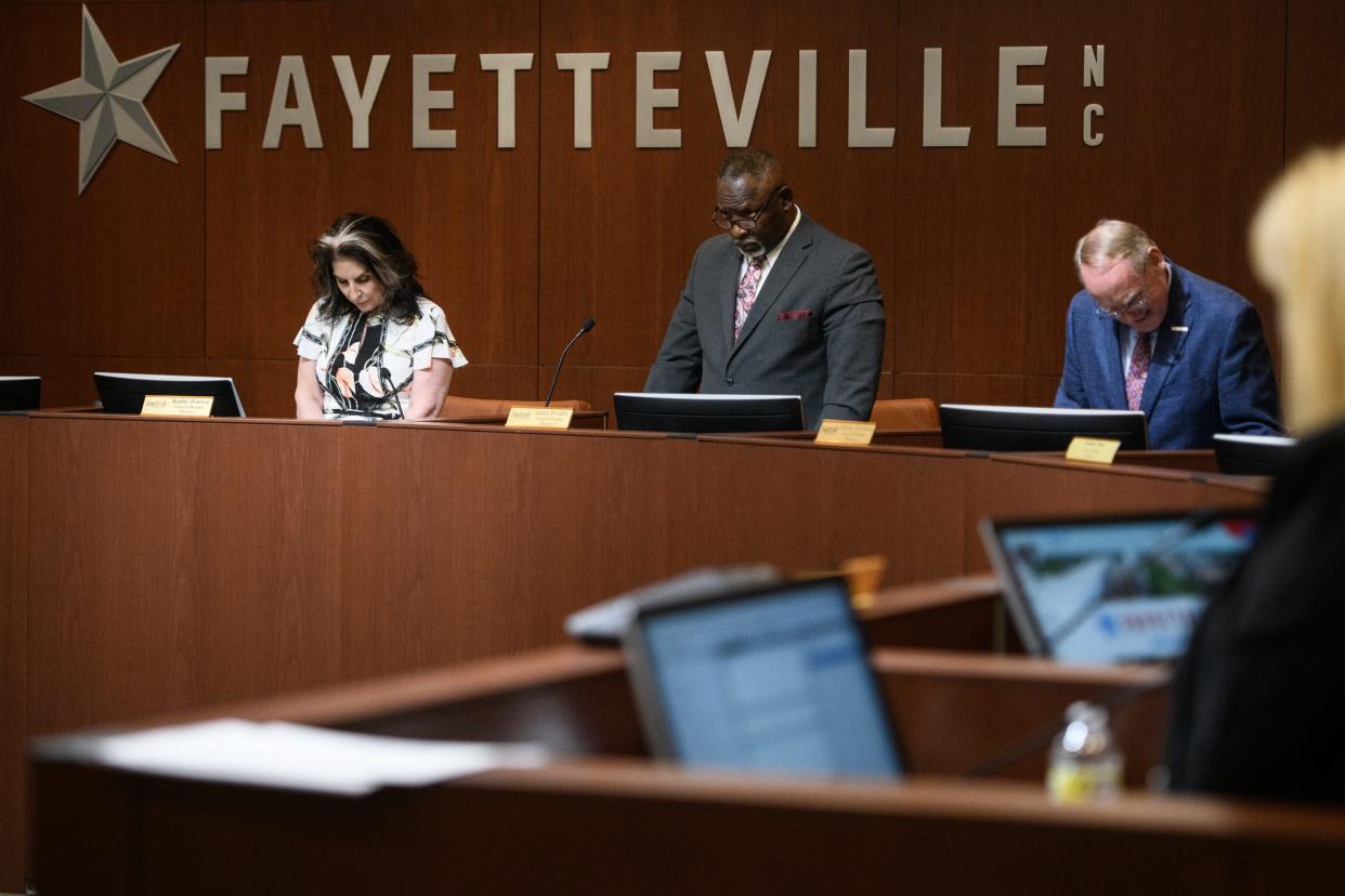 Mayor Pro Tem Kathy Jensen, left to right, council member Larry Wright and council member Johnny Dawkins bow their heads in prayer at a Fayetteville City Council meeting on Monday, April 25, 2022.