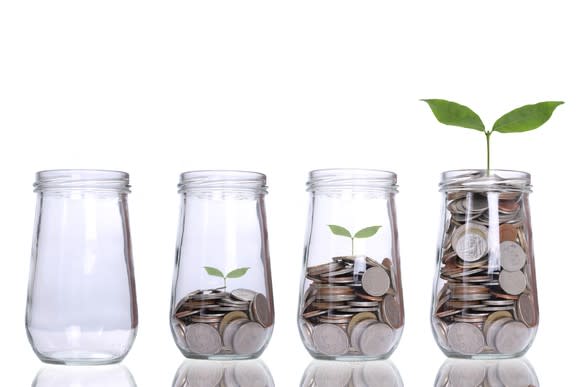 A row of four jars that are increasingly full of coins. The last jar is full and has a plant beginning to grow out of it.