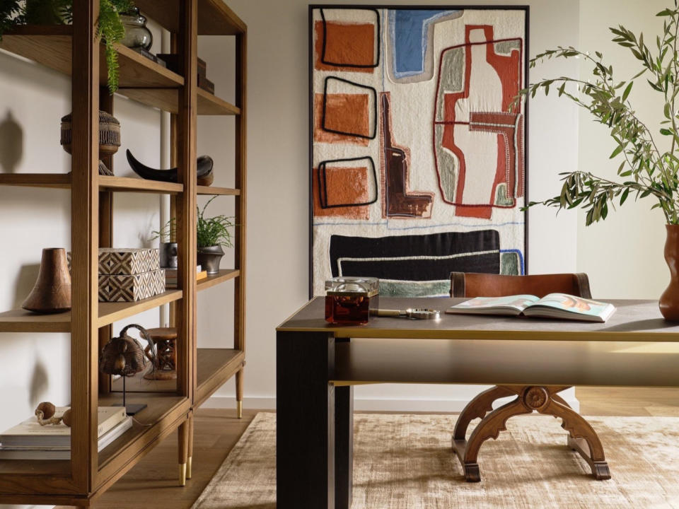 Home office with wood open shelving against a neutral background, large abstract artwork in earthy colours and a wood desk and chair