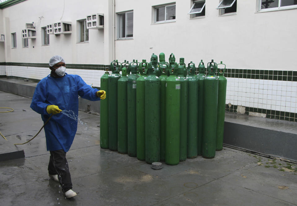 A health worker cleans the area where empty oxygen tanks stand idle at Joventina Dias Hospital in Manaus, Brazil, Friday, Jan. 15, 2021. Hospital staff and relatives of COVID-19 patients rushed to provide facilities with oxygen tanks just flown into the city as doctors chose which patients would breathe amid dwindling stocks and an effort to airlift some of them to other states. (AP Photo/Edmar Barros)