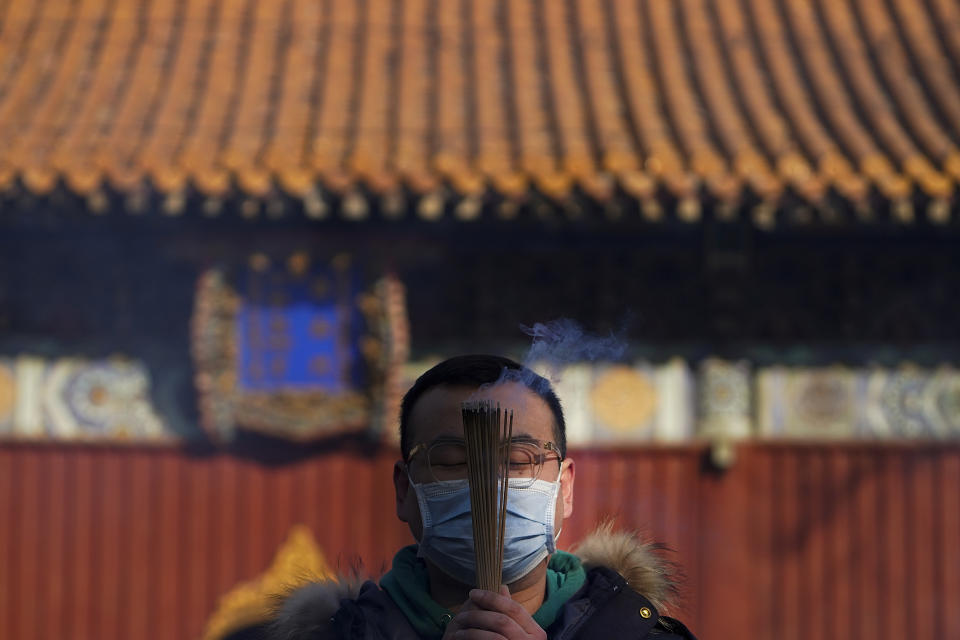 A man wearing a face mask to help curb the spread of the coronavirus holds incense offers prayers on the first day of the New Year at Yonghegong Lama Temple in Beijing, Friday, Jan. 1, 2021. President Xi Jinping said in a New Year address that China has made major progress in developing its economy and eradicating rural poverty over the past year despite the coronavirus pandemic. (AP Photo/Andy Wong)