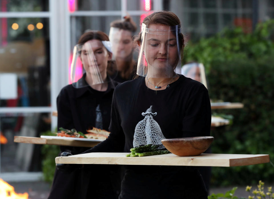 Servers are seen with protective gear carrying food at a restaurant in the Netherlands (Picture: Reuters)