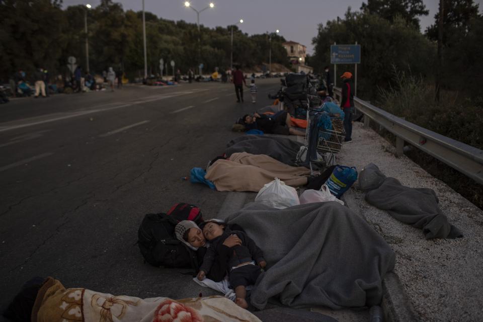 Migrants sleep on the road near the Moria refugee camp on the northeastern island of Lesbos, Greece, Thursday, Sept. 10, 2020. A second fire in Greece's notoriously overcrowded Moria refugee camp destroyed nearly everything that had been spared in the original blaze, Greece's migration ministry said Thursday, leaving thousands more people in need of emergency housing. (AP Photo/Petros Giannakouris)