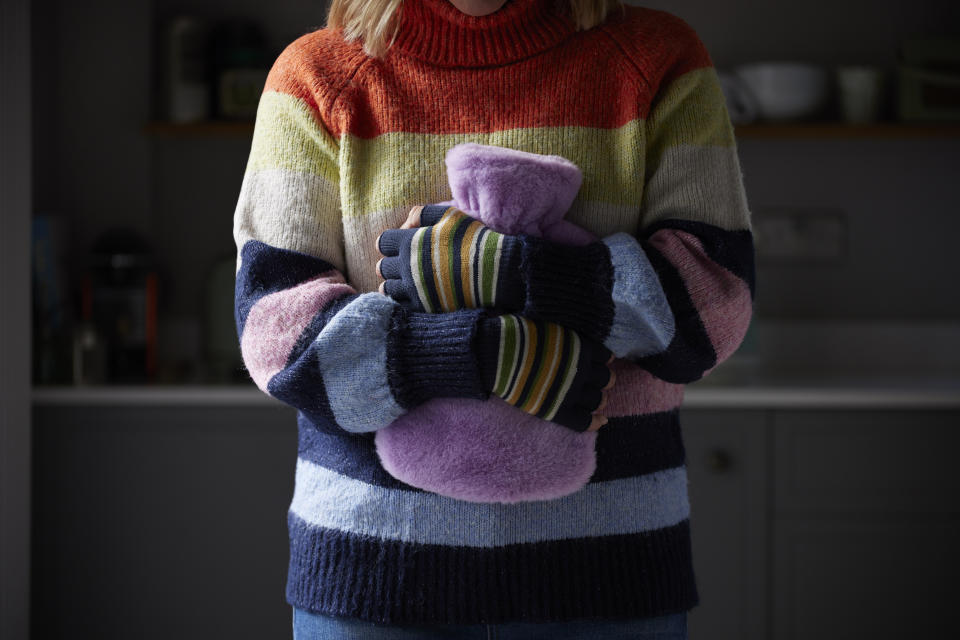 Woman wearing a jumper and holding a hot water bottle at home.