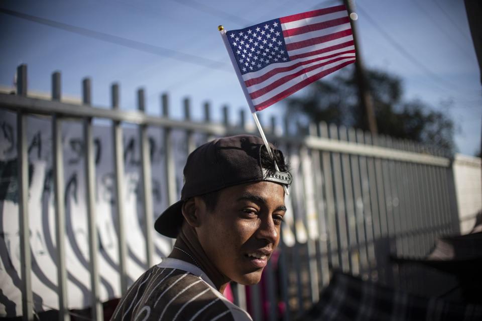 <p>A Central American migrant wanting to reach the United States in hopes of a better life, carries a US flag on his cap as he remains at a shelter in Tijuana, Baja California State, Mexico, near the US-Mexico border fence, on November 23, 2018.</p>