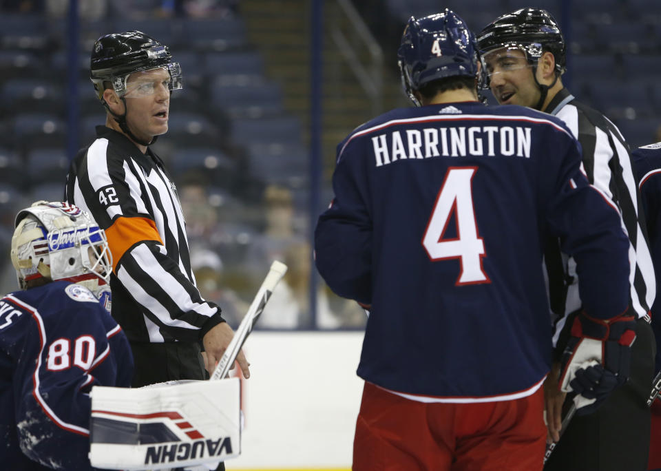 FILE - Referee Corey Syvret, top left, and linesman Andrew Smith, right, talk with Columbus Blue Jackets goalie Matiss Kivlenieks, bottom left, and Scott Harrington during the first period of the team's preseason NHL hockey game against the Buffalo Sabres on Monday, Sept. 17, 2018, in Columbus, Ohio. Syvret is a former minor league player who transitioned to a job he never thought he'd want. (AP Photo/Jay LaPrete, File)