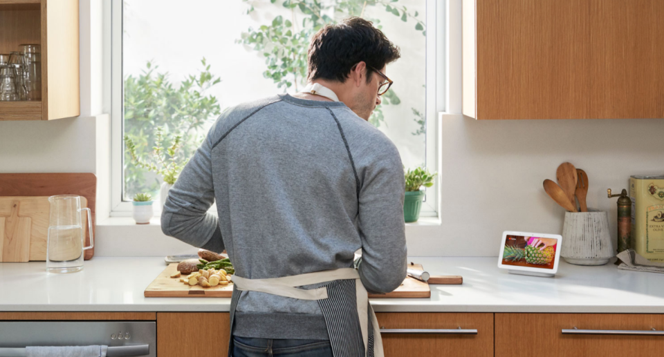 man cooking in kitchen wearing apron looking at google nest device