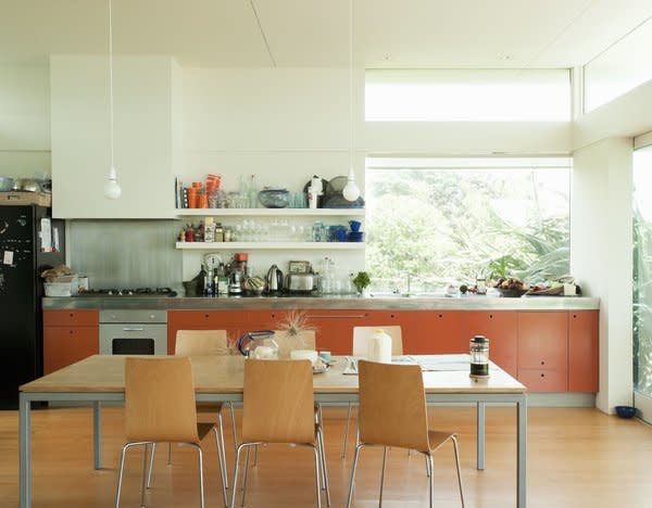 If you don't like handles sticking out from your cabinet doors, then one quirky and clever idea is to have a hole drilled near the top of the cabinet door, so you can stick you finger in it and pull the door open. These orange-painted MDF cabinets in a New Zealand beach house is an example of how this idea works brilliantly in cheery, low- kitchen.