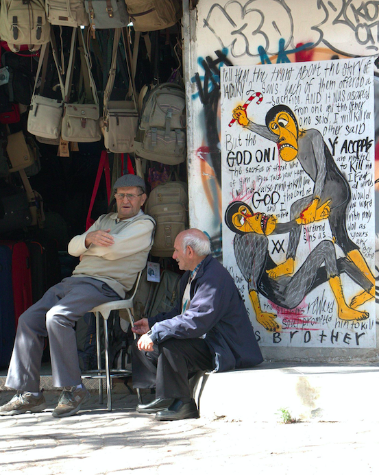 Two market sellers in front of a sign that may tell of their less friendly future in Tel Aviv, Israel.