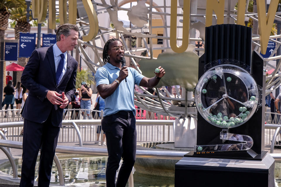 California Governor Gavin Newsom, left, looks on as Access Hollywood personality Scott Evans draws a ball with a winning number during the Vax for the Win lottery contest at Universal Studios in Universal City, Calif., Tuesday, June 15, 2021. Starting Tuesday, there were no more state rules on social distancing, and no more limits on capacity at restaurants, bars, supermarkets, gyms, stadiums or anywhere else. (AP Photo/Ringo H.W. Chiu)