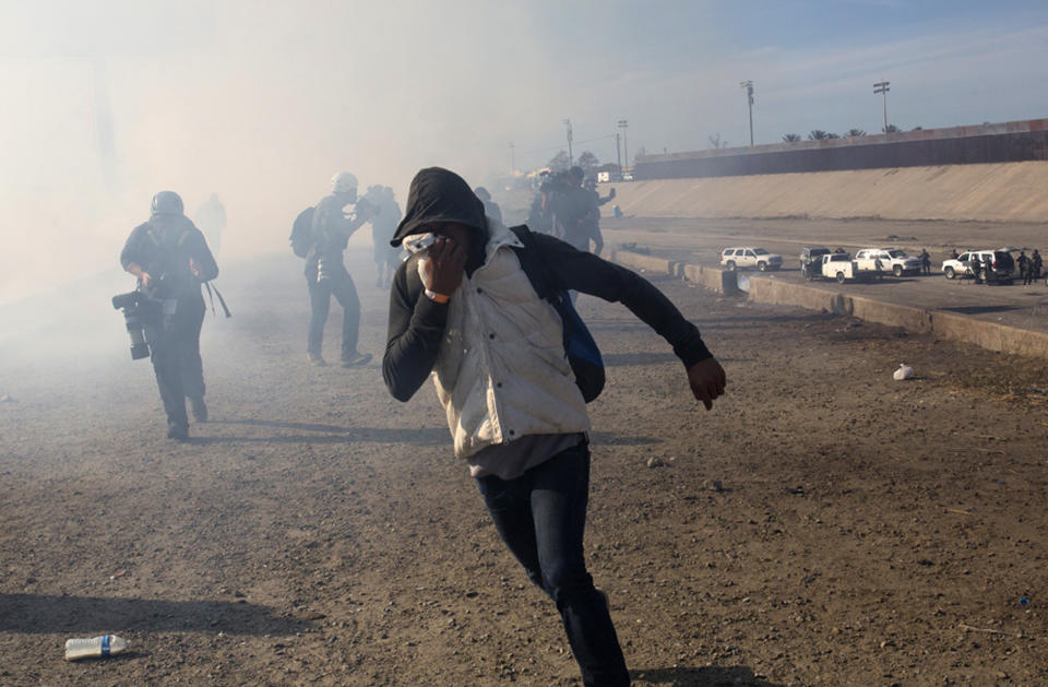 FILE - In this Nov. 25, 2018 file photo, a migrant runs from tear gas launched by U.S. agents, amid members of the press covering the Mexico-U.S. border, after a group of migrants got past Mexican police at the Chaparral crossing in Tijuana, Mexico. A San Diego TV station says the U.S. government ran an operation to screen journalists, activists and others while investigating last year's migrant caravan from Mexico. KNSD-TV says documents leaked by a Homeland Security source show a January database listing at least 10 journalists, seven of them U.S. citizens, as warranting secondary screening at U.S. points of entry. (AP Photo/Rodrigo Abd, File)