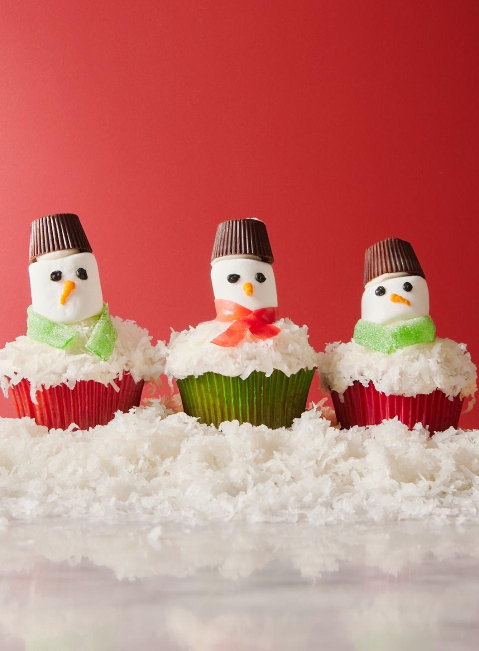 snowman cupcakes topped with shredded coconut snow, marshmallow faces, candy scarves, and peanut butter cup hats