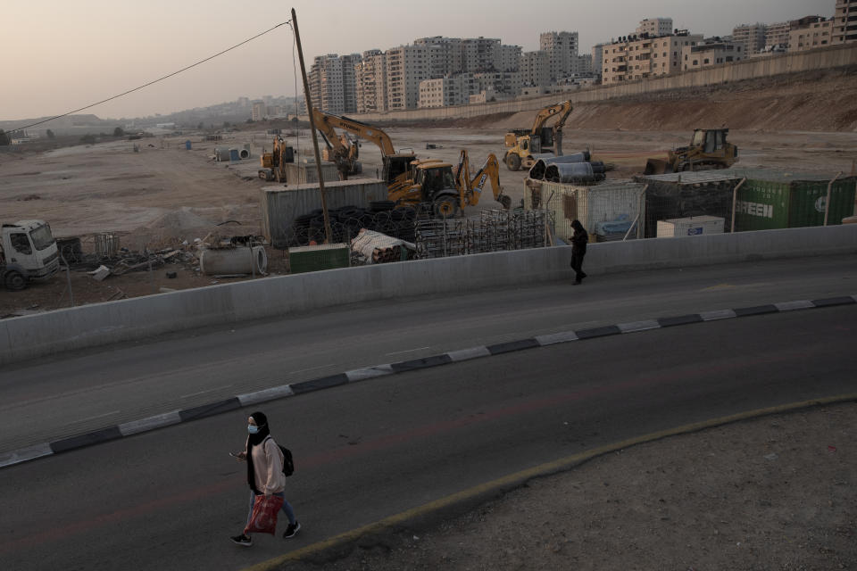 A woman leaves the Qalandia checkpoint to the West Bank from Jerusalem Wednesday, Nov. 24, 2021. Behind her is the the controversial separation barrier, right, and the site where Israel is moving ahead with plans to build a massive Jewish settlement on the site of a long-abandoned airport that the Palestinians had hoped would one day service their future capital in east Jerusalem. (AP Photo/Maya Alleruzzo)