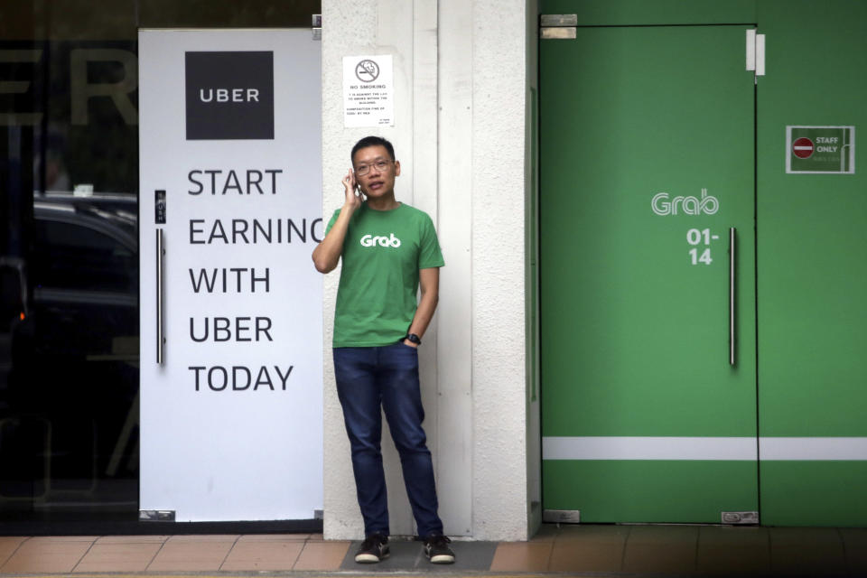 A man speaking on his mobile phone while standing between Grab and Uber offices during lunch hour on Monday (26 March). (PHOTO: Associated Press)