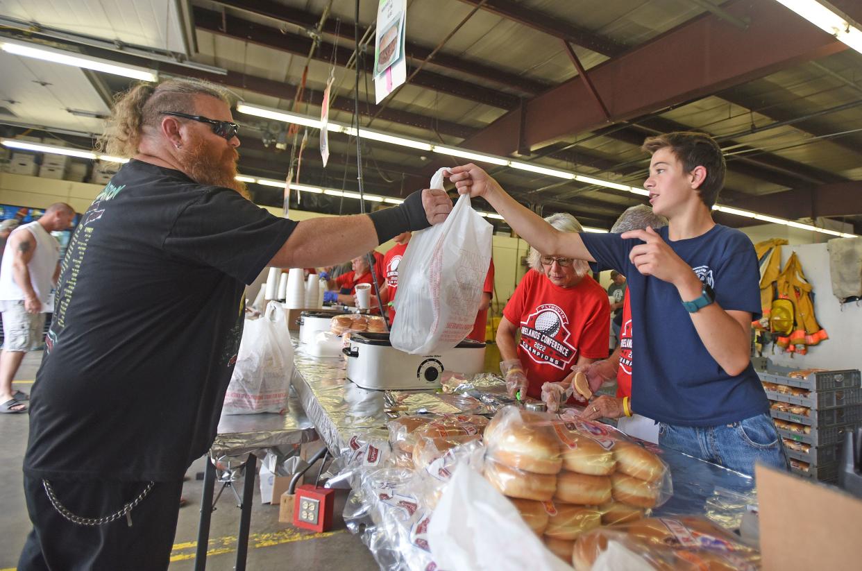 Logan Garman, 14 years old, serves a bag of sandwiches to a customer Friday afternoon during the Shiloh Ox Roast.