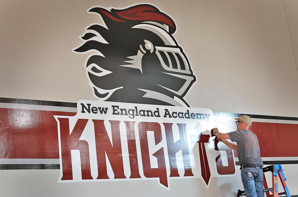Paul Lyden installs the Knights logo in the gymnasium of New England Academy.