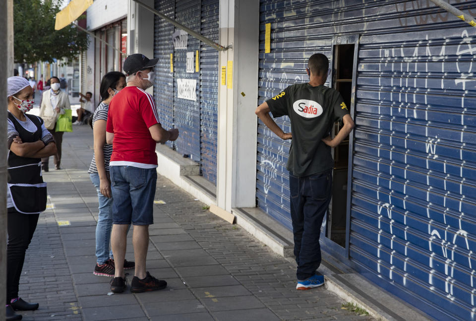 Clientes esperando para recoger artículos comprados por internet, en una tienda parcialmente abierta durante la cuarentena impuesta para contener los contagios del nuevo coronavirus, en Sao Paulo, Brasil, el lunes 1 de junio de 2020. (AP Foto/Andre Penner)