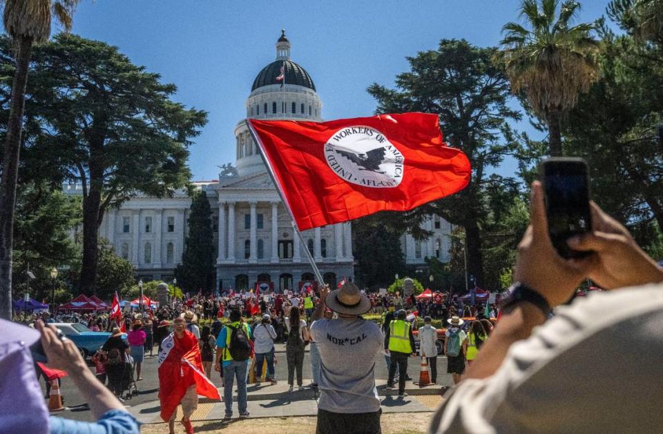 Joe Aguilar de Sacramento ondea una bandera de United Farm Workers frente al Capitolio estatal en Sacramento, después de que el sindicato terminó una marcha de 24 días el viernes 26 de agosto de 2022, para pedir al gobernador Gavin Newsom que firme un proyecto de ley que daría a los trabajadores agrícolas la posibilidad de votar desde casa para sindicalizarse.