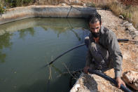 Nazih Sabra sets a tube to pump water from an artificial pond at Harf Beit Hasna village in Dinnieh province, north Lebanon, Wednesday, Sept. 7, 2022. Farmers in a small mountainous town in Lebanon's northern Dinnieh province once could rely on rain to irrigate their crops and sustain a living. But climate change and the country's crippling economic crisis has left their soil dry and their produce left to rot. (AP Photo/Hussein Malla)