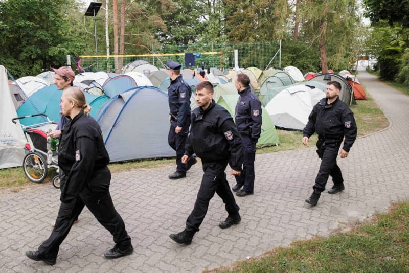 Police officers patrol tents at the protest camp on the edge of protests against Tesla. After violent clashes at the Tesla factory site in Gruenheide near Berlin, the police are preparing for further demonstrations on Saturday. Carsten Koall/dpa