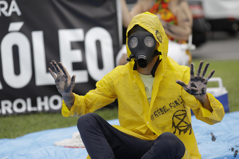 A demonstrator with his hands darkened with black paint and wearing a gas mask protests against the auction for the exploration of oil fields close to Abrolhos, a marine national park in Bahia state, in Rio de Janeiro, Brazil, Thursday, Oct. 10, 2019. Under pressure from environmental organizations, none of the 17 companies involved in the process presented any offers. (AP Photo/Silvia Izquierdo)