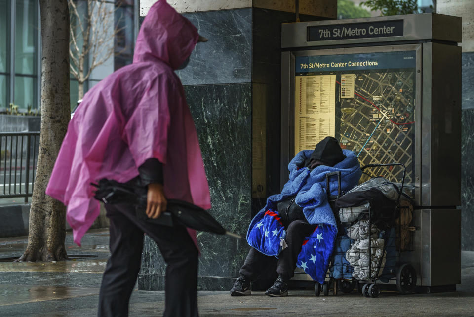 A homeless person, right, outside the entrance to a subway station in downtown Los Angeles