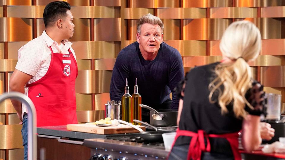 Gordon Ramsay in a blue shirt leans over a stove on 