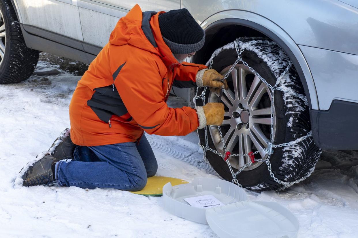 A medium shot of a senior, Caucasian man fixing snow chains onto his car tyres.