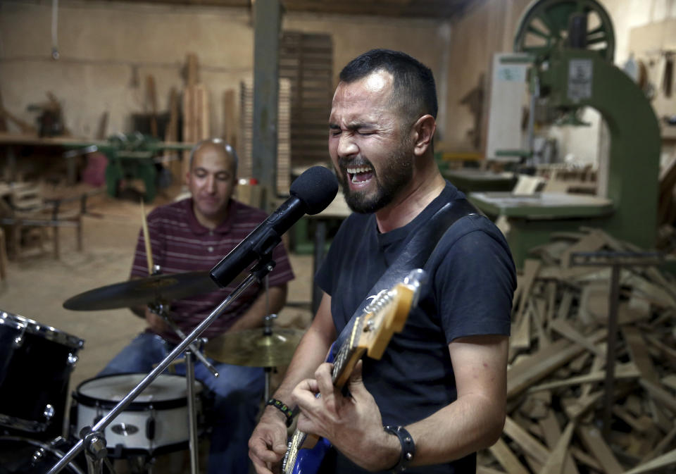 In this July 20, 2018 photo, Afghan musician Hakim Ebrahimi, a member of the Arikayn rock band, plays at a furniture workshop in Eslamshahr, on the outskirts of Iran’s capital, Tehran. The band, made up of Afghan migrants, plays Metallica-inspired ballads about the struggles of millions of Afghans who have fled to Iran to escape decades of war and unrest. In Iran they face discrimination, and have had to contend with hard-liners opposed to Western culture. (AP Photo/Ebrahim Noroozi)