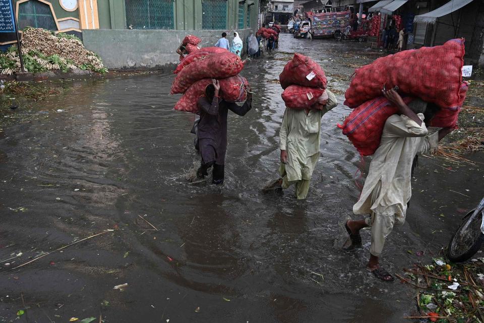 Labourers carry sacks of potato as they wade amid a flooded market in Lahore (AFP via Getty Images)