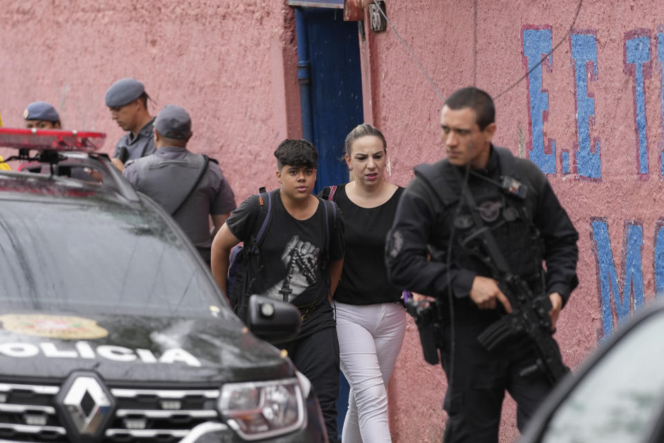 A student leaves the Thomazia Montoro school with his mother, as they walk past security forces, after a fatal stabbing at the school in Sao Paulo, Brazil, Monday, March 27, 2023. A 13-year-old student fatally stabbed a 71-year-old teacher and wounded three teachers and two fellow students Monday in a knife attack at the public school, state officials said. (AP Photo/Andre Penner)