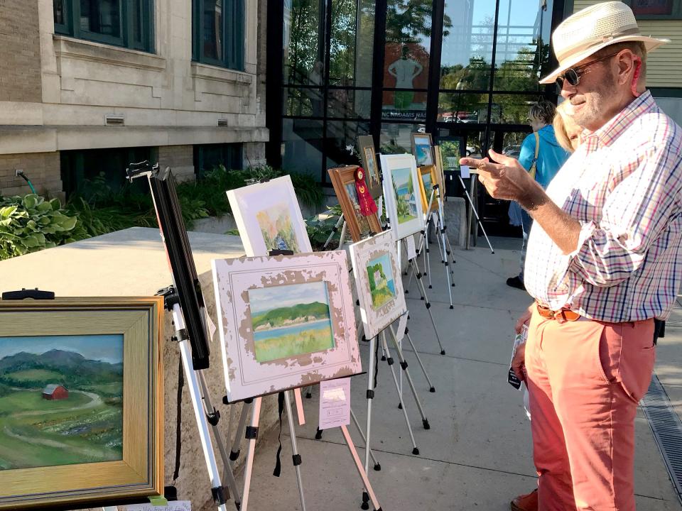 People admire plein air paintings set up outside of the Crooked Tree Arts Center in Petoskey during the annual Art Walk event on Thursday, Aug. 31, 2023.