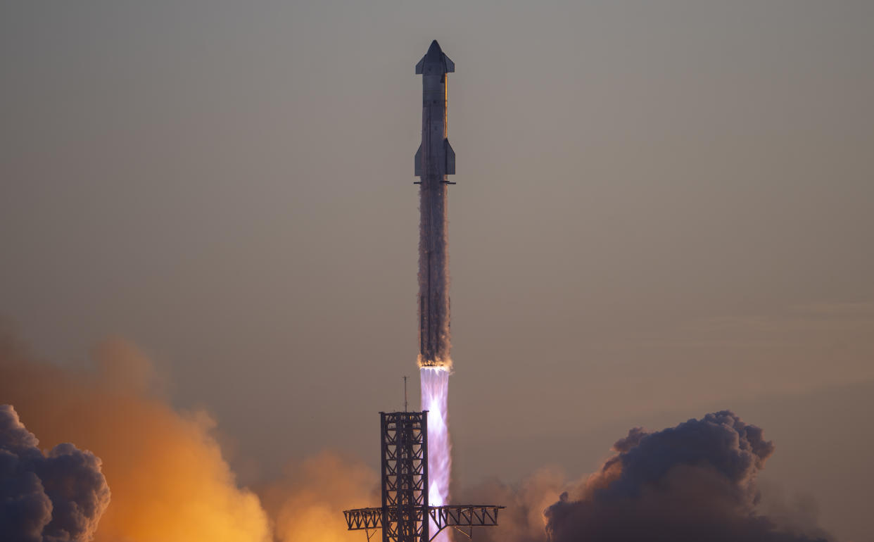  A giant rocket lifts off at sunrise with its fins and booster in silhouette. 